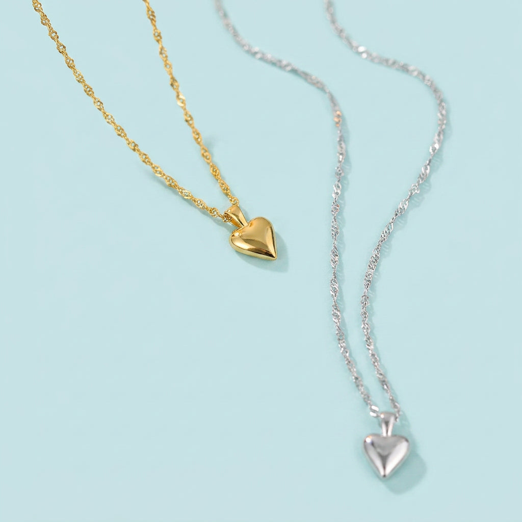 Gold and silver heart pendant necklaces angled view, pale blue background